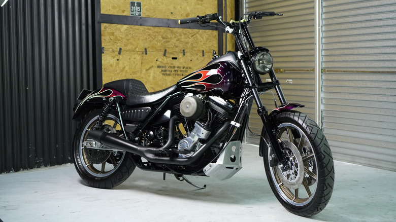A customized Harley-Davidson FXR motorcycle with black and flame paint job, parked in an indoor garage studio