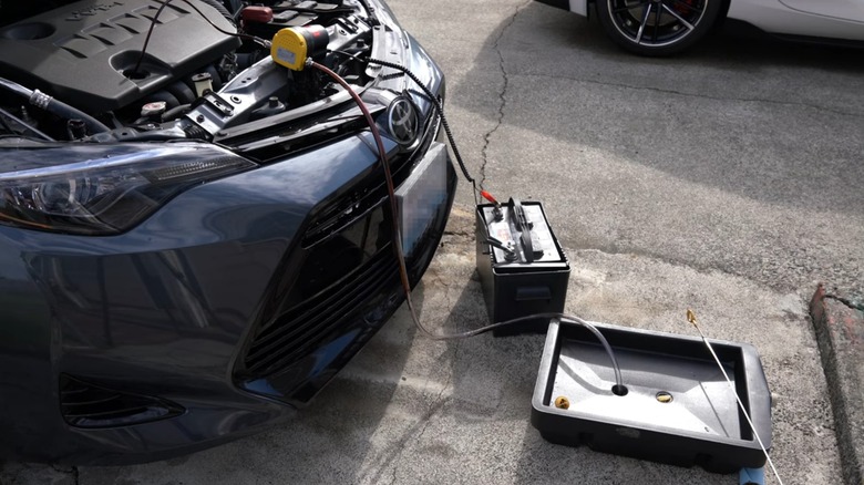 a person using an electric oil extractor connected to a car battery to replace engine oil