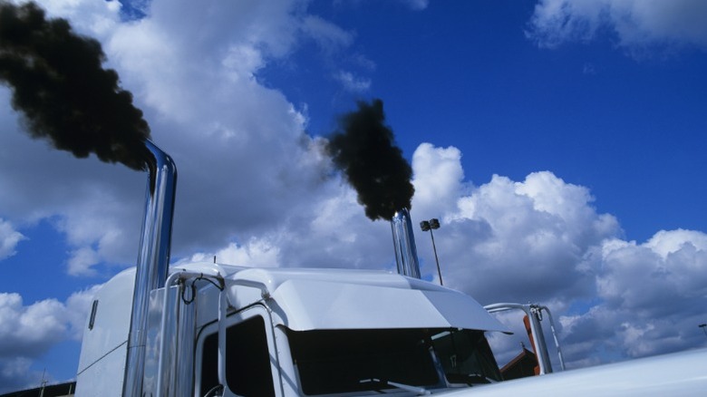 A diesel semi truck emitting large clouds of black (sooty) exhuast