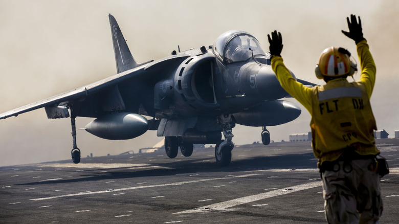 An AV-8B hovers above a carrier deck