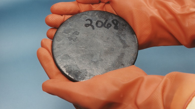 Two gloved hands holding a billet of highly enriched uranium with the number 2068 written on it