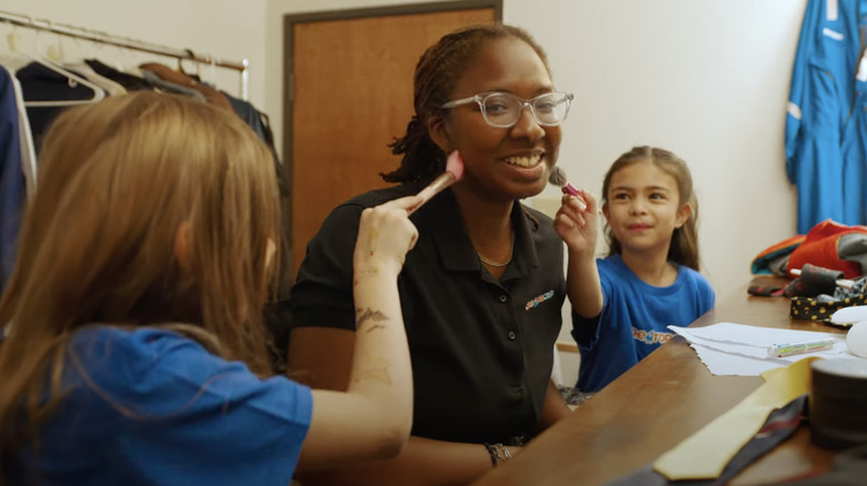 Creator Camp kids applying makeup to counselor's face with brushes