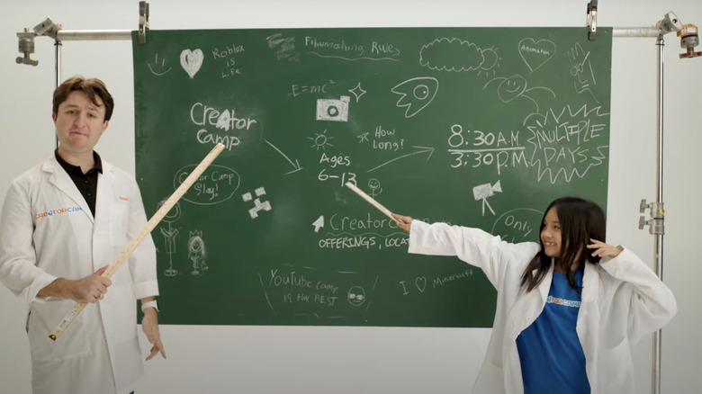 man and girl in lab coats presenting Creator Camp on chalkboard