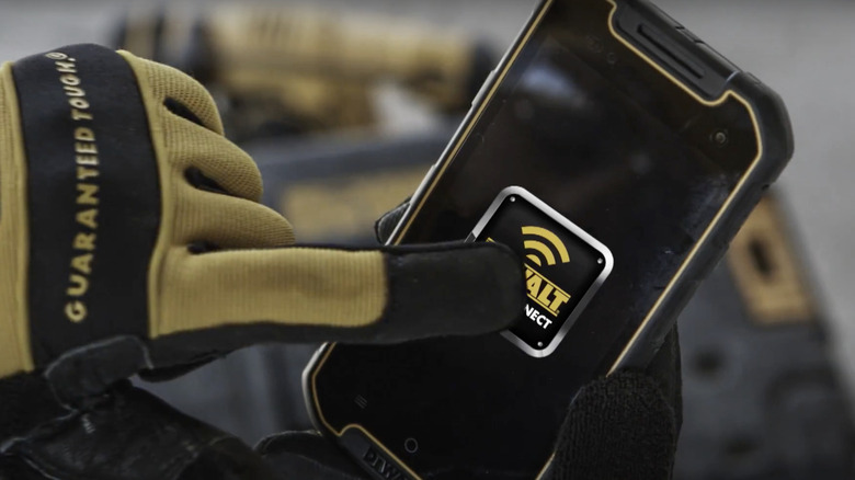 A gloved hand touching the screen of the DeWalt rugged smartphone.