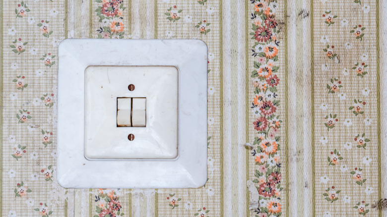An old white, push button light switch on a flowered wallpapered wall