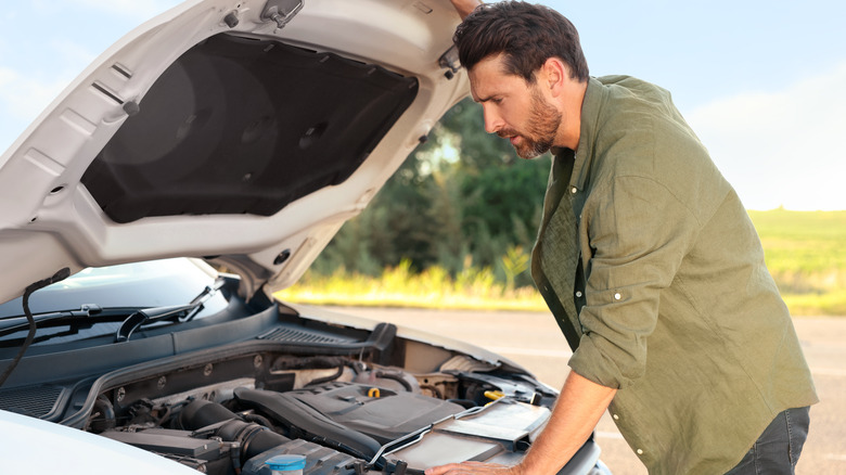 A driver looking under the hood of a broken car