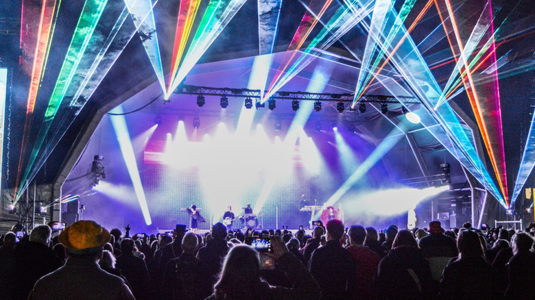 Laser beams fanning over a concert crowd as a fan films the show on a phone