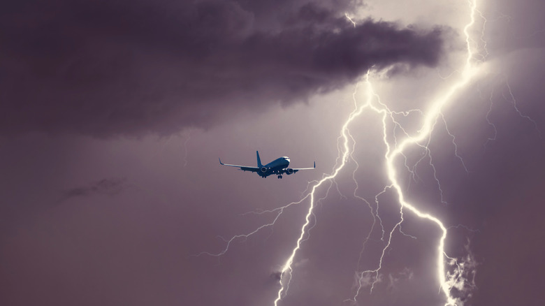 Passenger jet in the sky with lightning in the background.