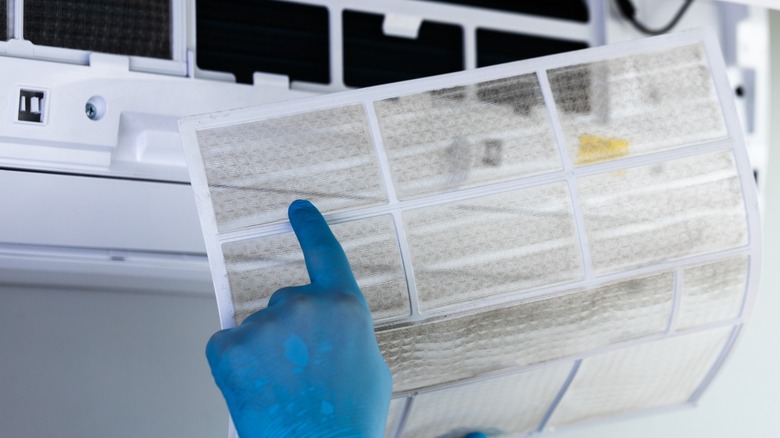 Person wearing blue gloves removing dirty filter from an air conditioning unit