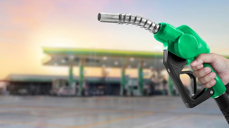 Hand holding green gas pump with filling station in background