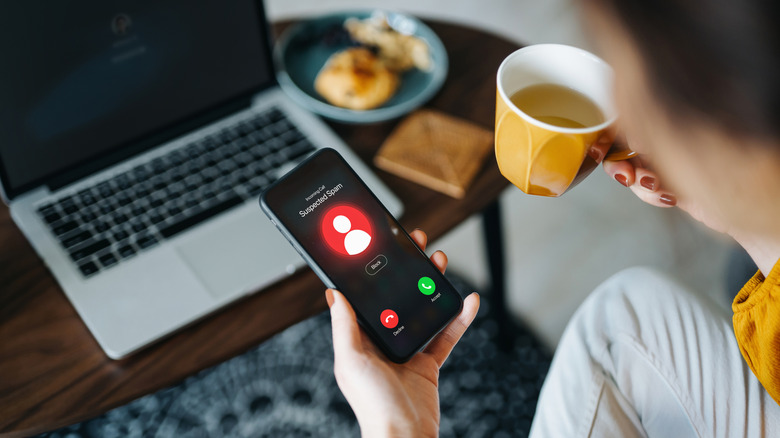Woman sitting in front of laptop while looking at phone with scam call