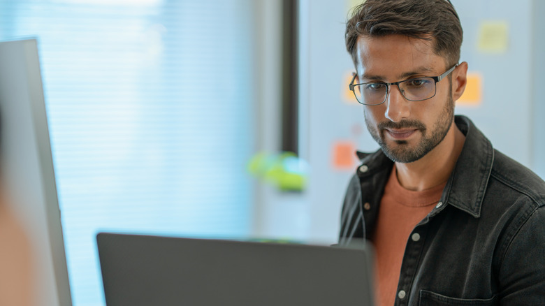 A man with glasses using a computer in an office space.