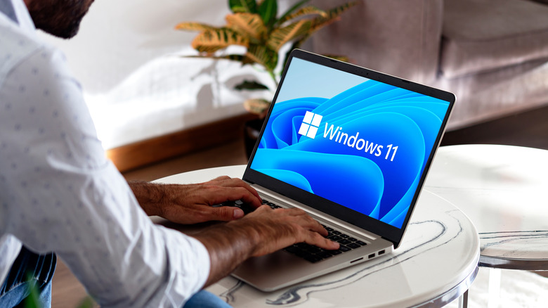 A man places his hands on the keyboard of a laptop with Windows 11 logo on the screen.