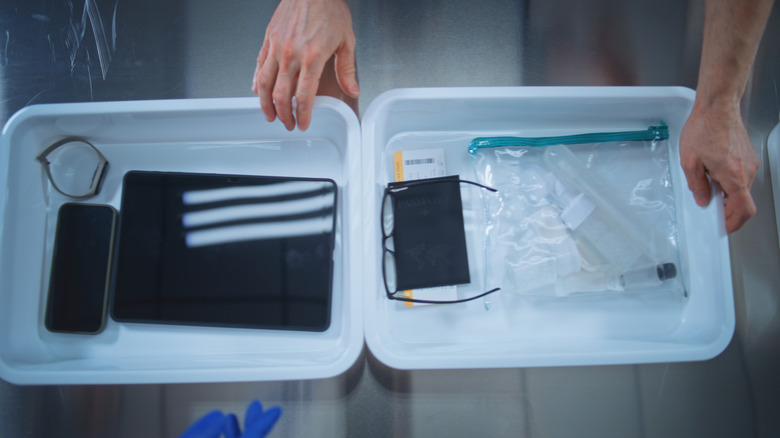 A passenger placing personal items into a plastic bin for TSA screening.