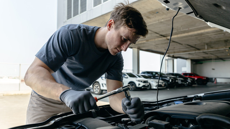 A mechanic working on an engine, various cars in the background