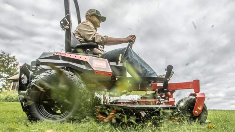 Man riding Toro riding mower with grass clippings flying around