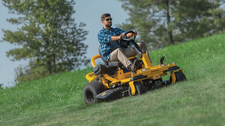 Man driving Cub Cadet riding mower on sloped yard