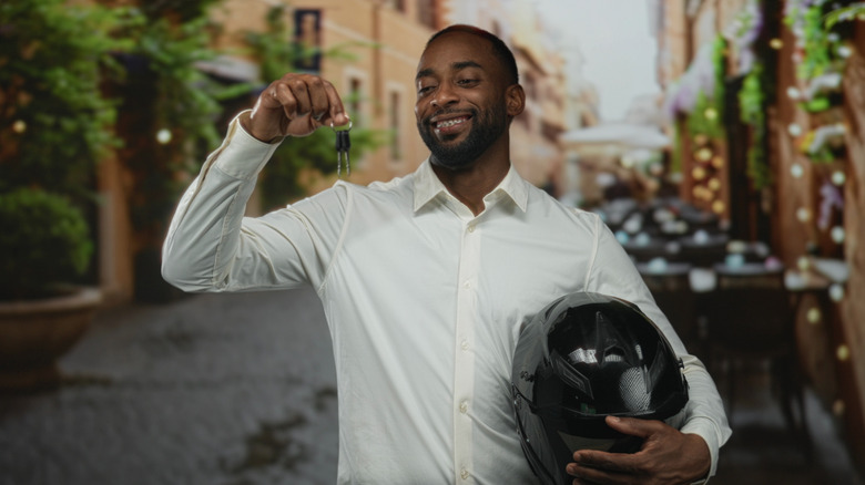 A person holding a motorcycle helmet and a set of keys.