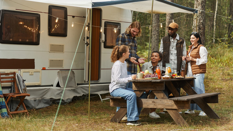 Young adults chatting around a table next to a camper trailer