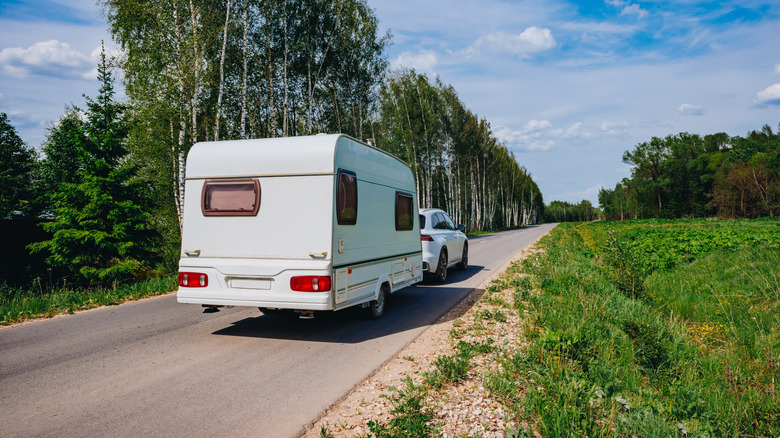 A white Genesis GV70 towing a white camper trailer, rear 3/4 view