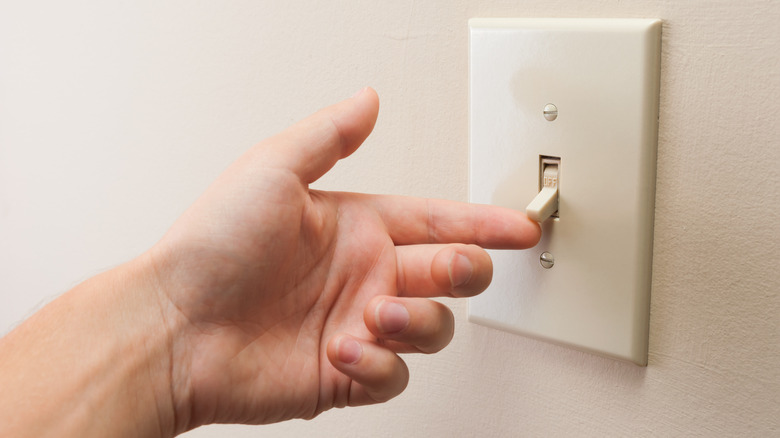 Hand turning wall light switch off