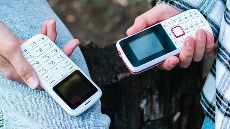 Two simple cell phones being held opposite each other by two people