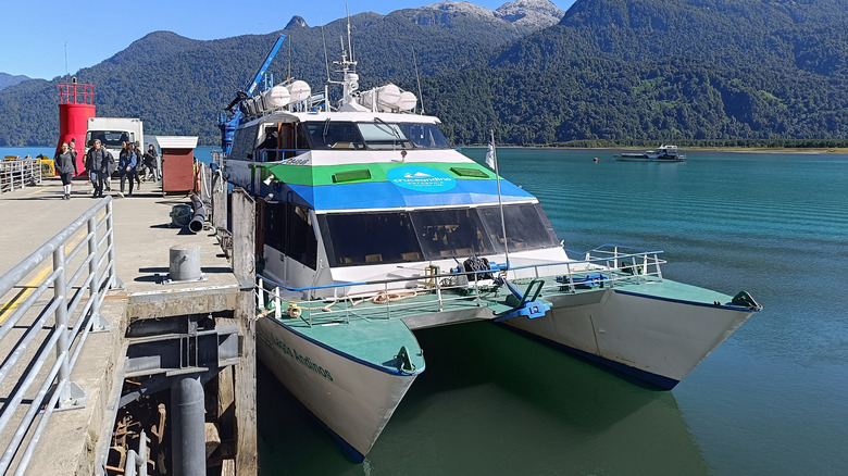 A catamaran docked at a port with mountains in the background
