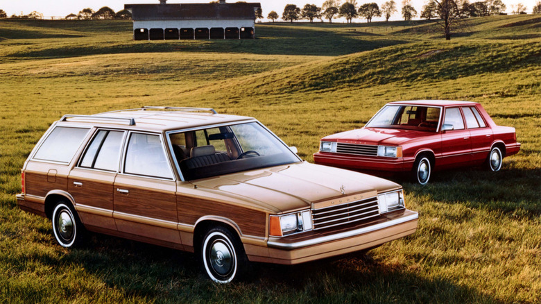 1984 Dodge Aries wagon and 4-door cars, wagon in-front with front-right view, 4-door behind with front-left view, parked on field