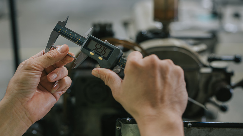a Person measuring a part with a caliper.