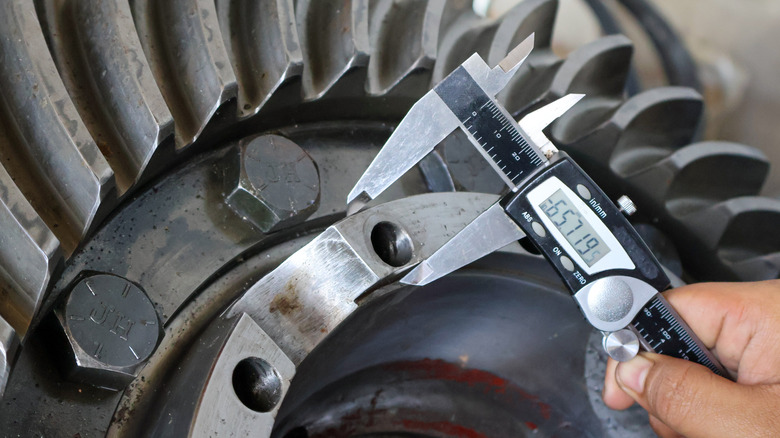 A person using a caliper to measure a machine part.