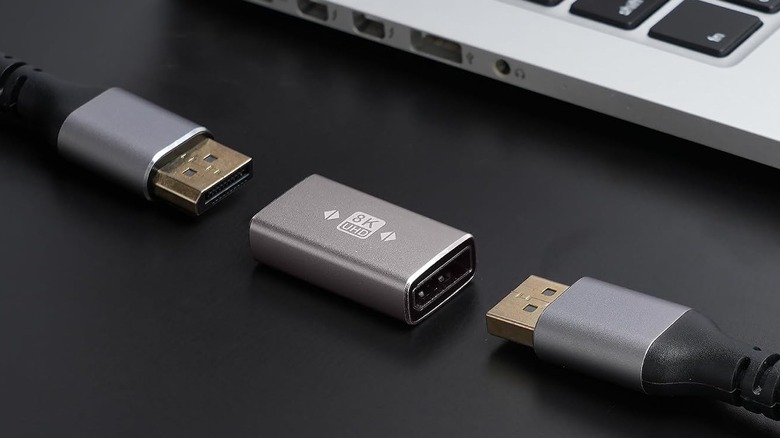 An 8K-rated DisplayPort coupler and two DP cables in front of a laptop keyboard