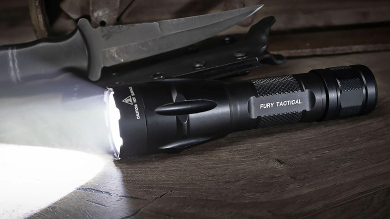 A black dual-fuel Fury flashlight emitting a white light on a table