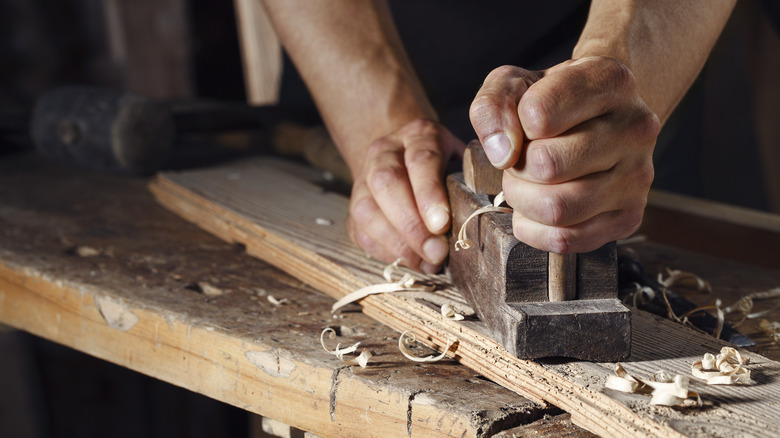 A woodworker uses a planer on a length of wood