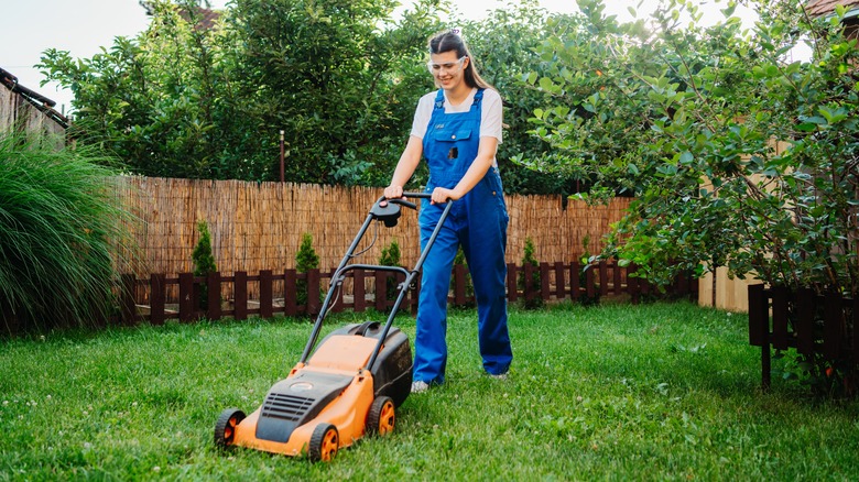 A young caucasian woman using a standard lawn mower in a backyard