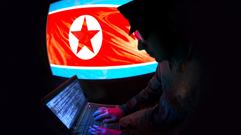 A North Korean hacker operates before the visage of a DPRK flag.