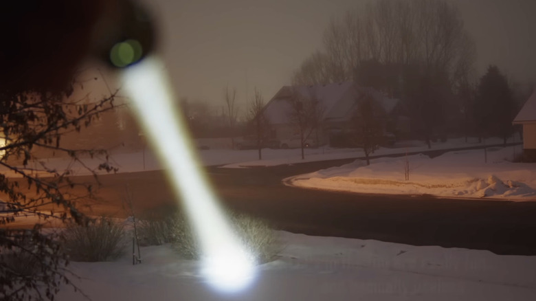A man pointing an LEP flashlight at snowy ground