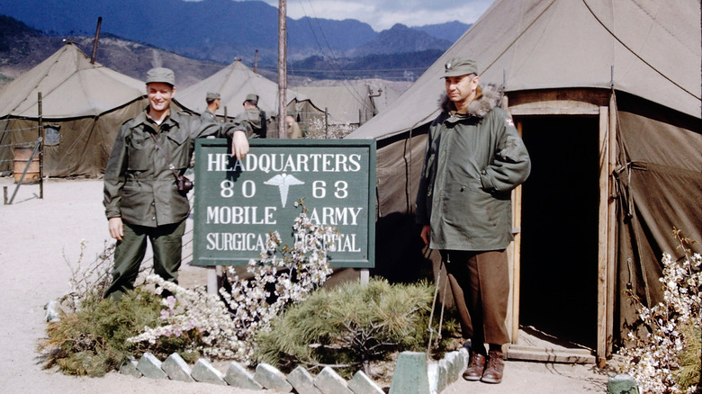 Dr Richard Warren and Colonel Jack Rush as they pose beside the sign outside the 8063rd MASH