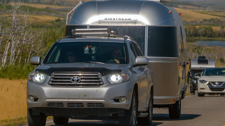 A silver Toyota Highlander SUV towing a classic Airstream trailer along a scenic highway