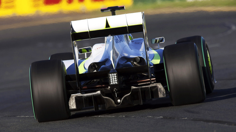 Rear view of an open-wheel race car negotiating a corner showing its black carbon fiber diffuser