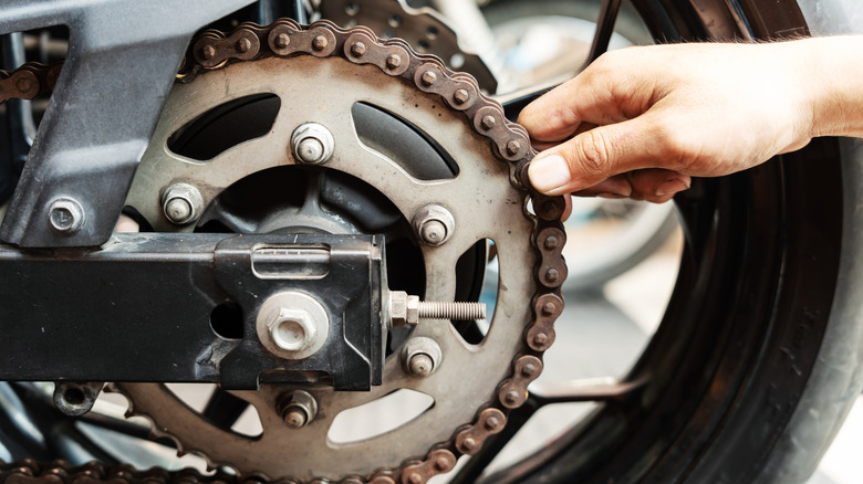 A hand pulls out the chain from the sprocket on a motorcycle rear wheel to check chain stretch.