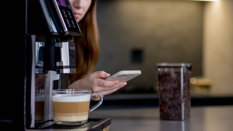 Woman on her phone while sitting next to smart coffee machine