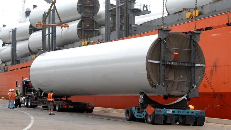 wind towers getting offloaded on a semi truck with a steer car in tow