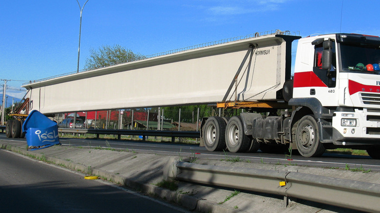 Trailer hauling a huge concrete beam with a steer car in tow