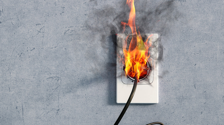 Fire and smoke coming out of a power cord connected to an electrical outlet