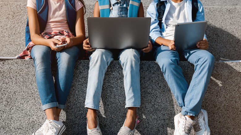 Imagem cortada para crianças da escola Meninos pré -adolescentes e garotas do ensino fundamental dos alunos sentados na escada e usando dispositivos digitais para gadgets sem fio Smartphone para tábuas de tablets ao ar livre na rua.