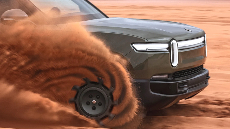 Wheel of Rivian truck spinning through sand