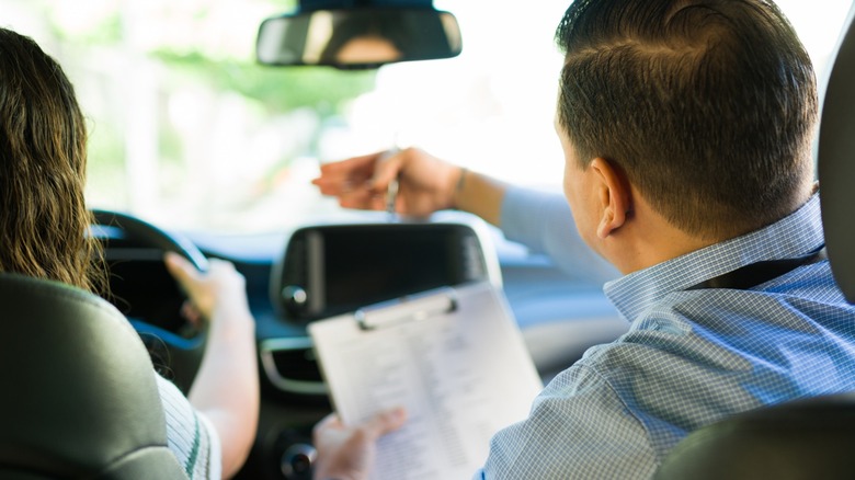driving instructor guiding teen student during driving test lesson