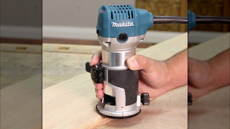 A person uses a Makita compact router on the side of a board