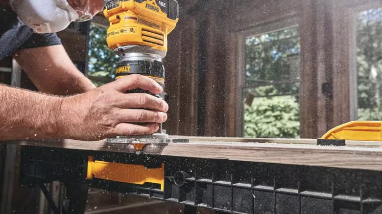 A person runs a DeWalt compact router along the side of a board