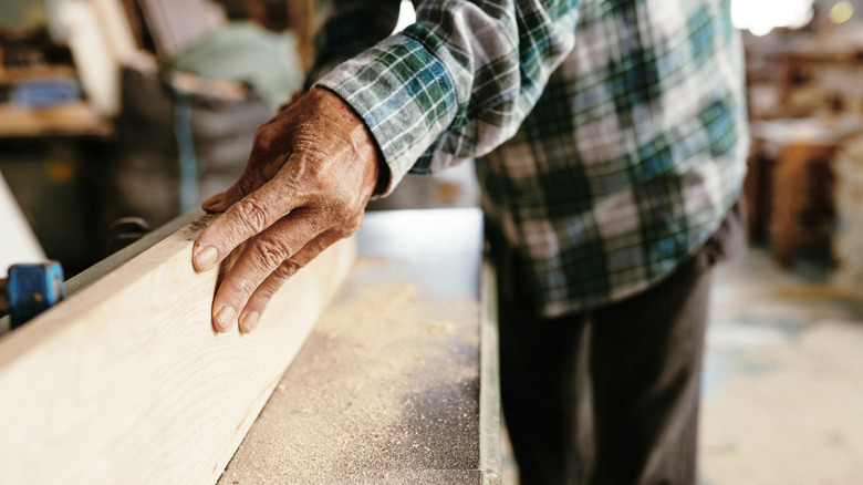 Close up of someone's hands planing a plank of wood using a large wood jointer